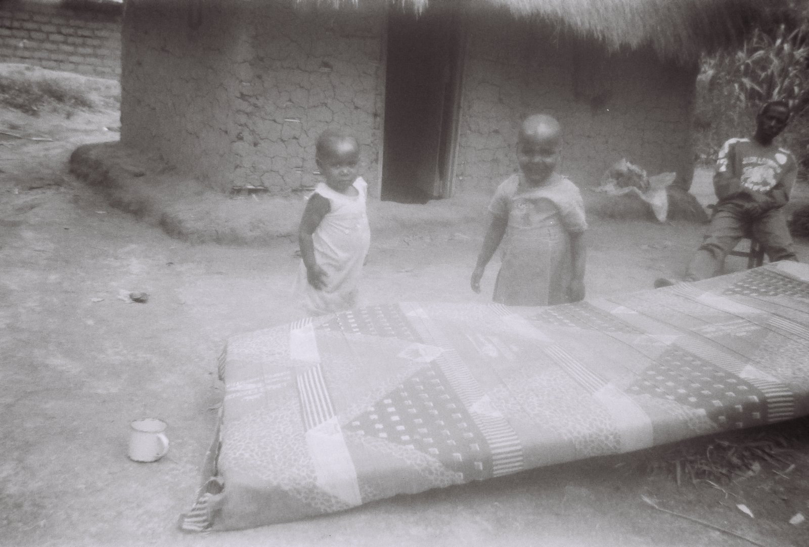 Congo Throwaway Camera Project with Eugene Ahn recycled the cameras for the Congolese Children to tell their stories. Dr. Danica Anderson when she was in the Congo DRC worked with the children and handed out the cameras to them. Returning periodically to pick up the film, Dr. Anderson collected their stories and images. In this family, the child photographer spoke of his father as sitting there but never there. Violence and substance abuse prevailed. The mother walked to water pump, worked the garden and dried the bricks for their hut. 